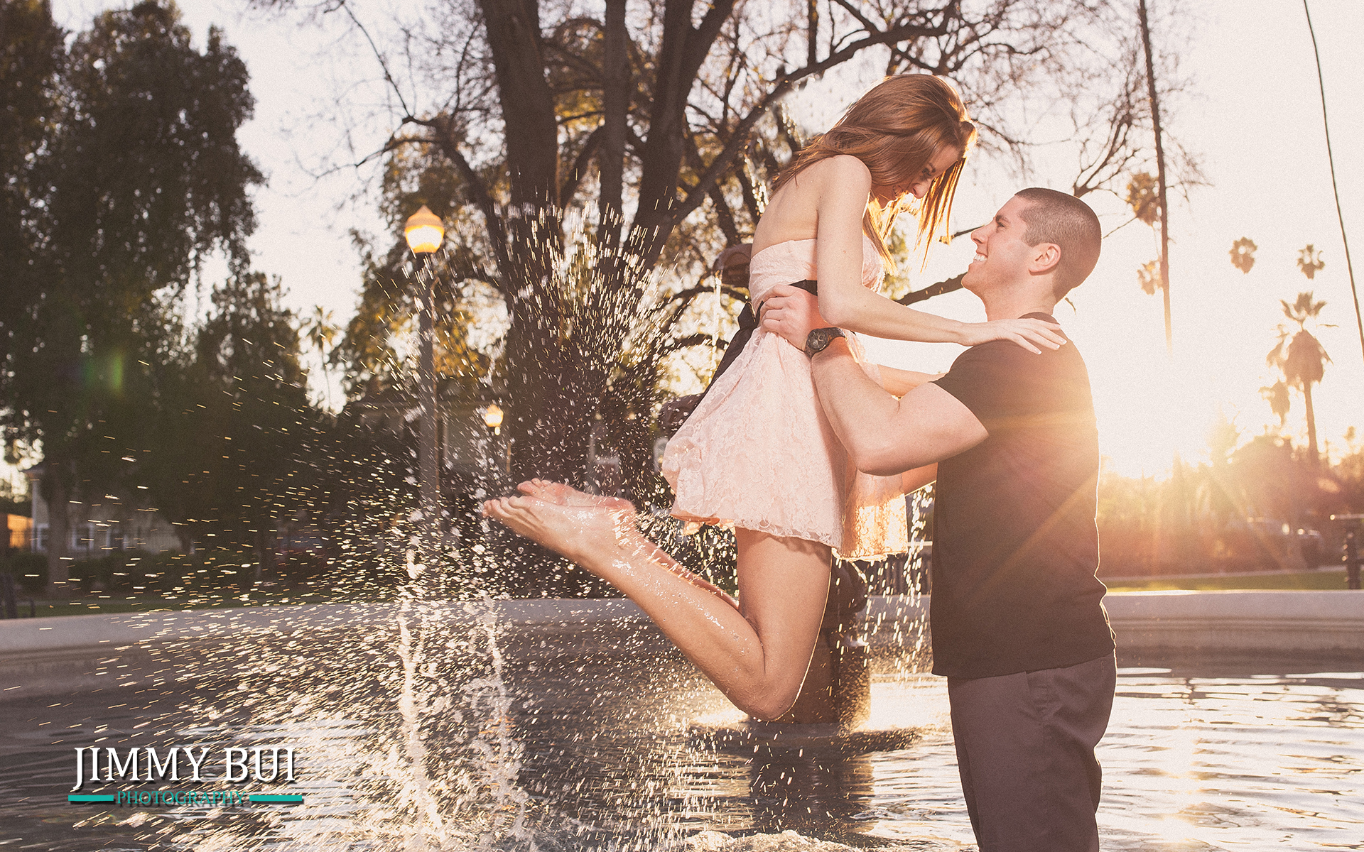man lifting fiance over fountain during sunset